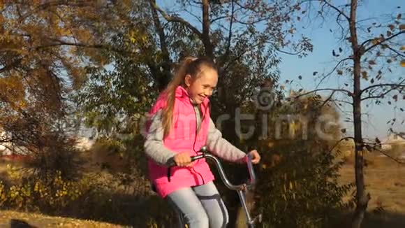 快乐的女孩骑着自行车在黄树背景下的秋天公园里微笑视频的预览图