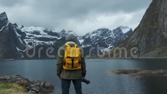 徒步旅行者欣赏雪山峰景带黄色背包的男性徒步旅行者的低角度后景享受视频的预览图