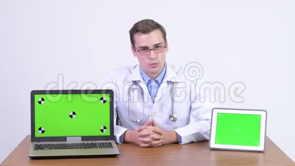 年轻英俊的男医生把笔记本电脑和数字平板电脑放在桌子上视频的预览图