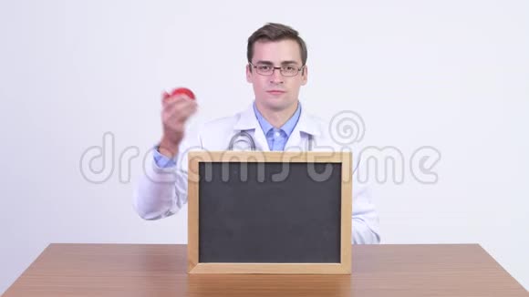 年轻快乐的帅哥医生拿着苹果对着木桌展示黑板视频的预览图