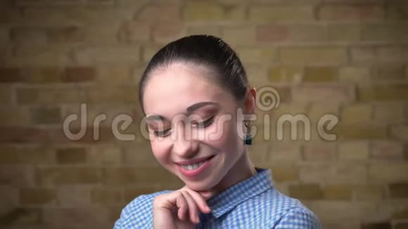白种人深色头发的女人的特写肖像马尾辫微笑地摆在布里克肯墙背景上的镜头上视频的预览图