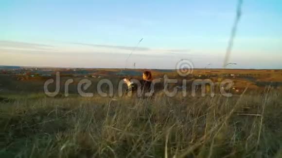 日落时分年轻女孩和美国斯塔福德郡的猎犬坐在草地上视频的预览图