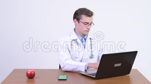 年轻快乐的帅哥医生对着木桌打电话视频的预览图