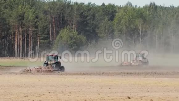 两台强力拖拉机在针叶林背景下在炎热的阳光天气下耕作干燥的土壤视频的预览图