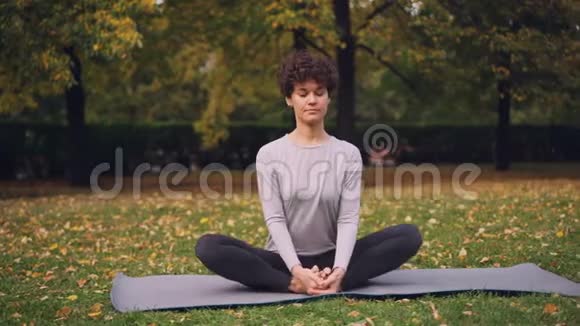漂亮的深色头发的女孩子在坐在瑜伽垫上姿势伸展双腿然后向前弯曲放松背部和身体视频的预览图