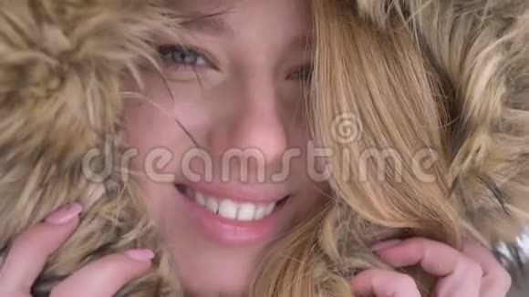 在冬天的街道上一幅可爱的年轻白种人女孩藏在毛皮罩里的特写肖像美丽地微笑着进入镜头视频的预览图