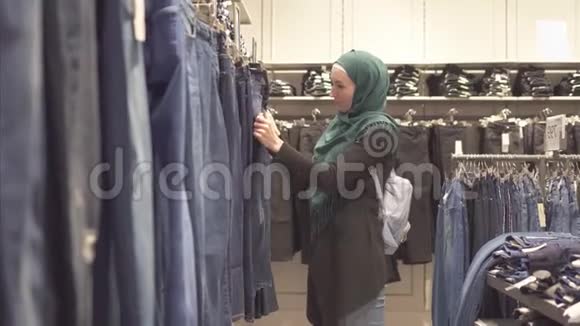 穿着头巾和背包的穆斯林妇女在商场的商店里选择牛仔裤视频的预览图