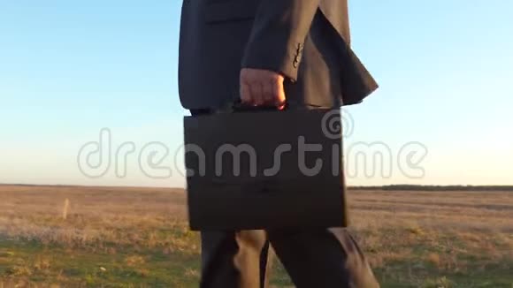 穿西装的商人去外地穿着商务服的男人手里拿着黑色公文包在公园里散步特写视频的预览图