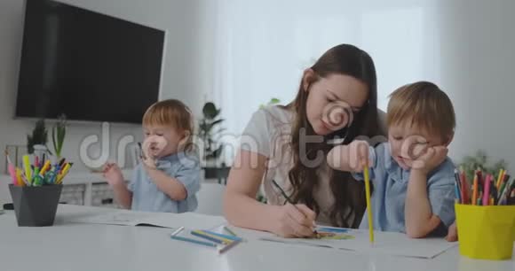 一位带着两个孩子在手机上说话的年轻母亲用铅笔画画并帮助孩子们用彩色画画视频的预览图
