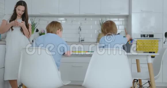 两个穿着蓝色衬衫的儿子坐在桌子旁在一张白色桌子旁的纸上画铅笔我妈妈写了一篇文章视频的预览图