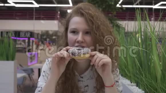 一个美丽的快乐女孩的肖像红发吃甜甜圈看着镜头视频的预览图