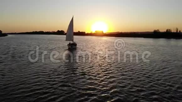 日落时分带着白帆的游艇沿着河游视频的预览图
