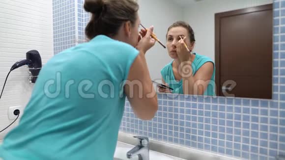 漂亮女人在浴室镜子前用眼影和化妆刷做眉毛化妆视频的预览图