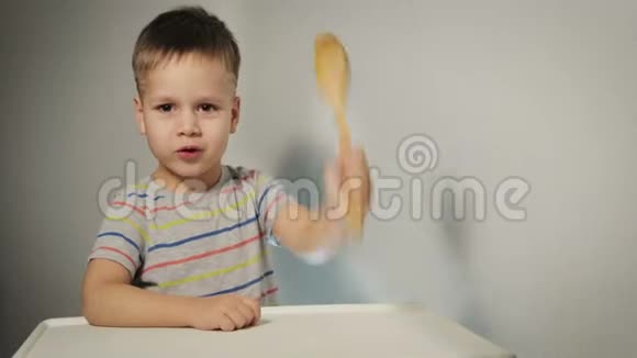 一个小而有趣的男孩敲着桌子上的勺子要求吃饭视频的预览图