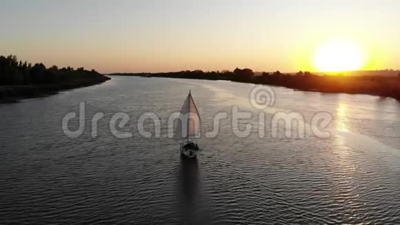 日落时分带着白帆的游艇沿着河游视频的预览图