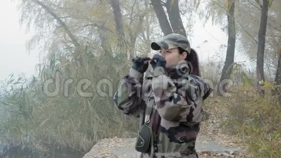 一位身着军服的美女伪装着双筒望远镜在雾中的河岸边观察四周视频的预览图