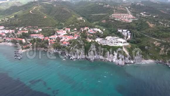 在希腊哈尔基迪基地区的旅游村和温泉设施下面有岩石的海上海岸鸟瞰图无人机视频的预览图
