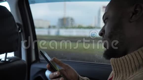 黑色男人浏览智能手机的肖像是在雨天在城市里骑汽车视频的预览图