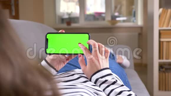 特写后景拍摄女性在手机上的浏览绿色屏幕水平地将其放在沙发上视频的预览图