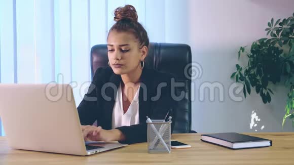 那个女孩坐在办公室用笔记本电脑打字时穿着时髦的衣服视频的预览图