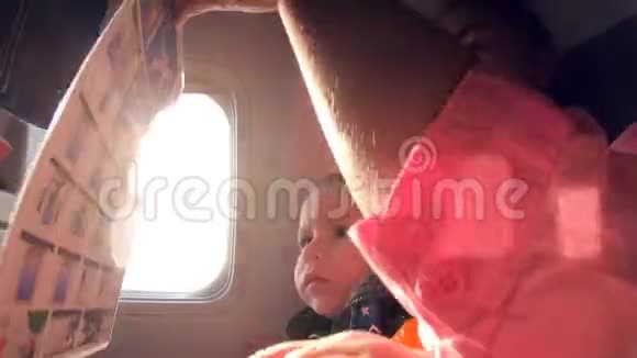 母亲带着孩子坐在靠近窗户的飞机上在阳光下飞行视频的预览图