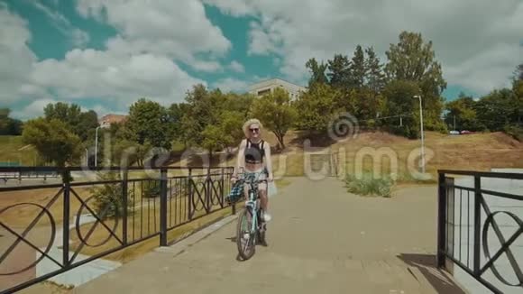 阳光明媚的夏日美丽的年轻女子骑着自行车微笑视频的预览图