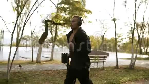平静的男人通过耳机跑步和听最喜欢的音乐早上在黑色绿色公园慢跑视频的预览图
