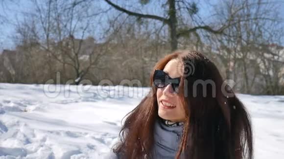 阳光明媚的一天戴着深色太阳镜的积极微笑的女人在公园的蓝天背景上打雪球视频的预览图