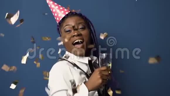 漂亮的非洲女孩戴着帽子手里拿着香槟酒杯一边玩着一边跳舞一边在纸屑上飞舞视频的预览图