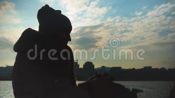 年轻女子在大海城市和天空的背景上拍摄日落视频的预览图