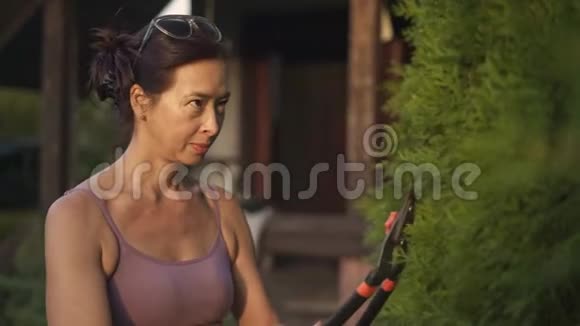 微笑的亚洲女人用剪刀在她的花园里剪树视频的预览图