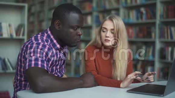 欧洲妇女和美国黑人男子带笔记本电脑在图书馆学习视频的预览图
