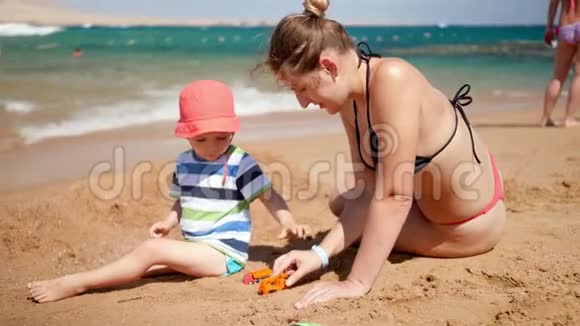 小母亲和她的孩子儿子在海边玩玩具车的4k视频夏季海滩家庭放松视频的预览图