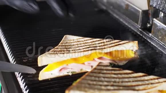 厨师用刀子从电烤架上取出热三明治视频的预览图