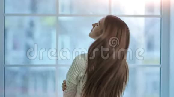 一个年轻的女人长着一头漂亮的长发望着冰冻的大窗户后景视频的预览图