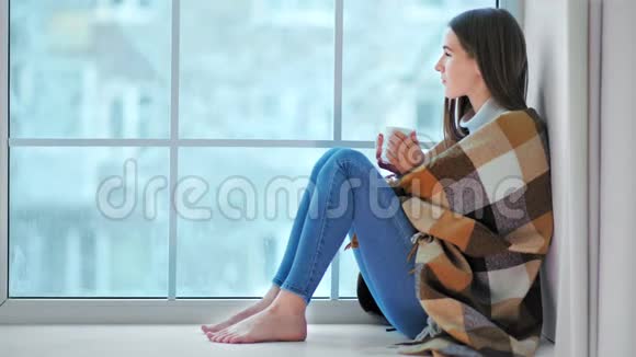 光着脚微笑的女人坐在窗台上看冬天的天气视频的预览图