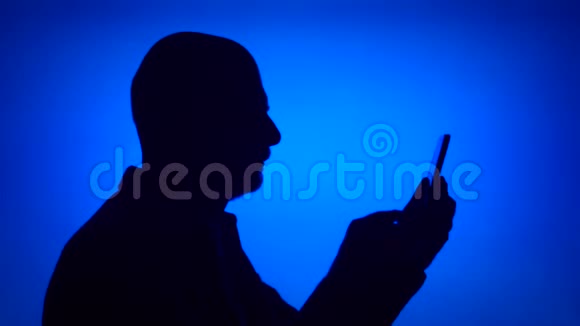 高级男士剪影在蓝色背景下使用手机男的脸型做自拍视频的预览图