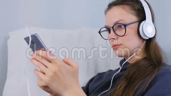 戴眼镜的女人在家里用耳机听音乐视频的预览图
