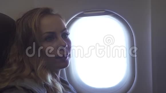 在飞机窗口背景上描绘年轻女子的肖像卷曲的女孩看着天空中飞行的飞机窗户女乘客视频的预览图