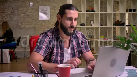 有着黑色长发和胡须的白种人男性集中精力在笔记本电脑上打字在挂着红杯子时喝酒视频的预览图
