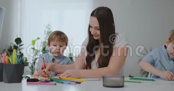 坐在客厅的桌子旁一位年轻的母亲教儿子拿铅笔教他画画视频的预览图