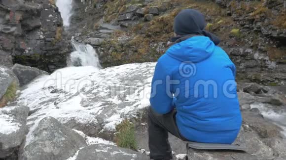 男性旅行者正在山里休息他坐在一个美丽的山瀑布附近放松和享受自然视频的预览图