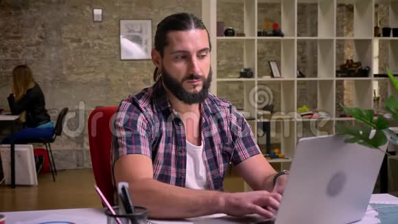 一个满脸黑胡子的白种人他看着笔记本电脑的屏幕坐在屏幕上满是思虑的怀疑视频的预览图