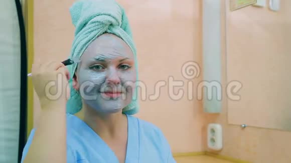 一个微笑的女人的脸头上有一条毛巾皮肤上有一刷蓝色的粘土平均计划视频的预览图