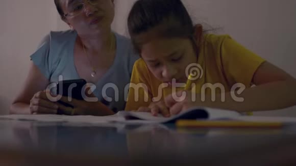 妈妈正在使用智能手机在书桌上给女儿教作业视频的预览图