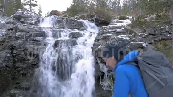 一个人带着背包沿着山区路线旅行他来到美丽的瀑布在一张自拍视频的预览图
