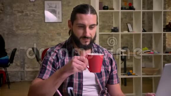 有胡子的创意工作者快乐的脸专注于在桌面上喝咖啡神情开朗视频的预览图