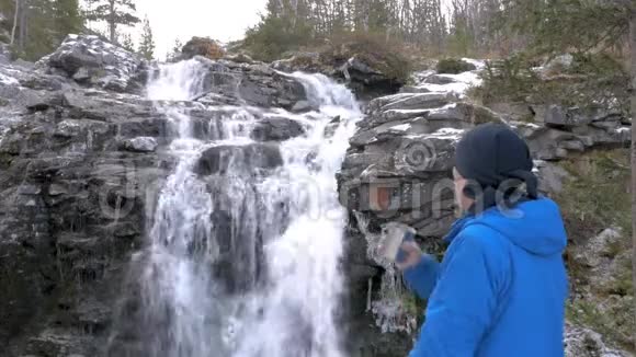 男性旅行者正在美丽的山瀑布下休息特写镜头他喝茶欣赏美丽的景色视频的预览图