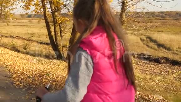 一个留着长发穿着粉红色夹克的年轻女孩在秋天公园骑自行车慢动作视频的预览图