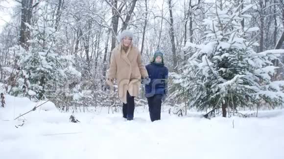 冬季乐趣和旅游理念母亲和儿子走在雪林里视频的预览图